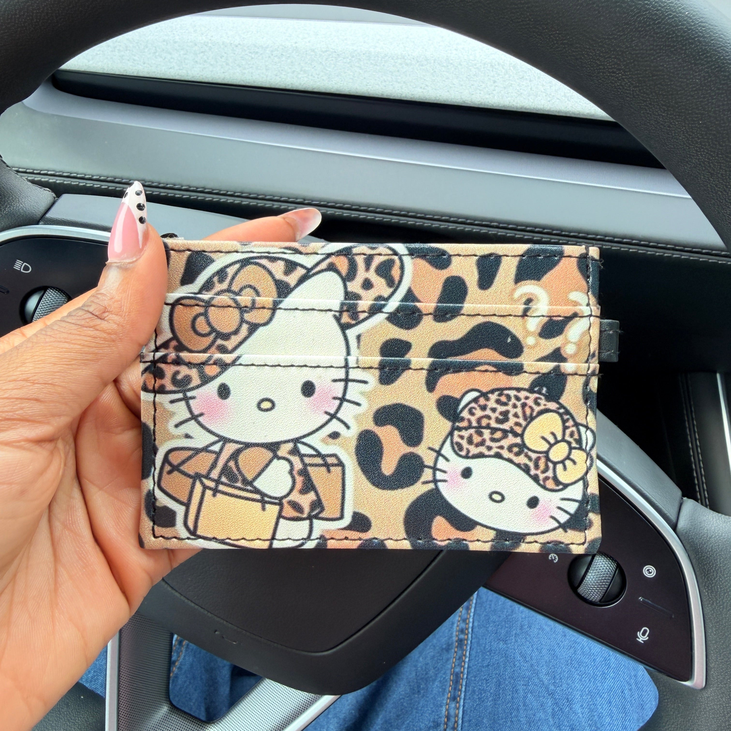 Hand holding a leopard print cardholder with cartoon character design in front of a car dashboard.